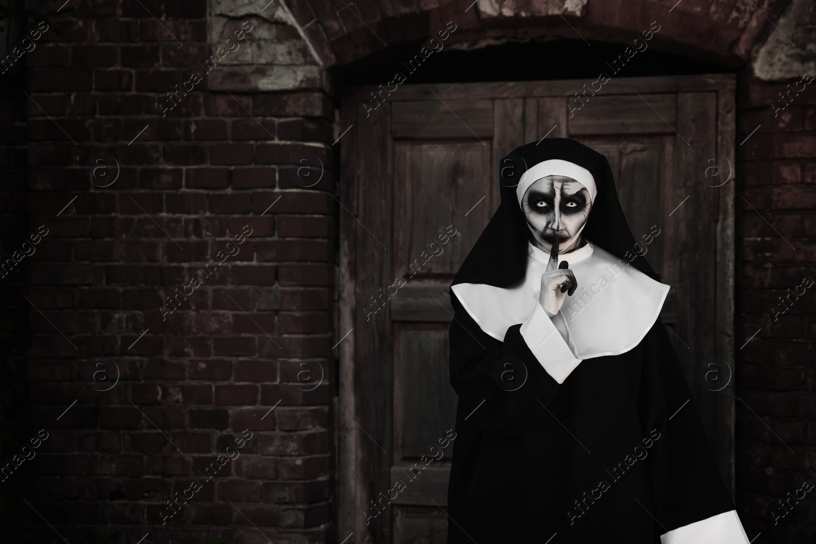 Photo of Portrait of scary devilish nun near red brick wall, space for text. Halloween party look