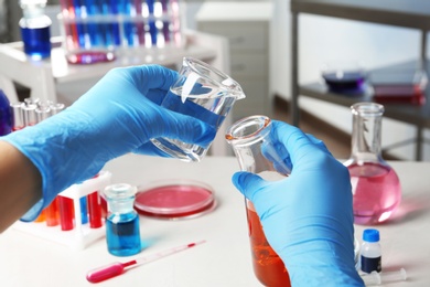 Photo of Scientist pouring reagent into beaker at table in chemistry laboratory, closeup