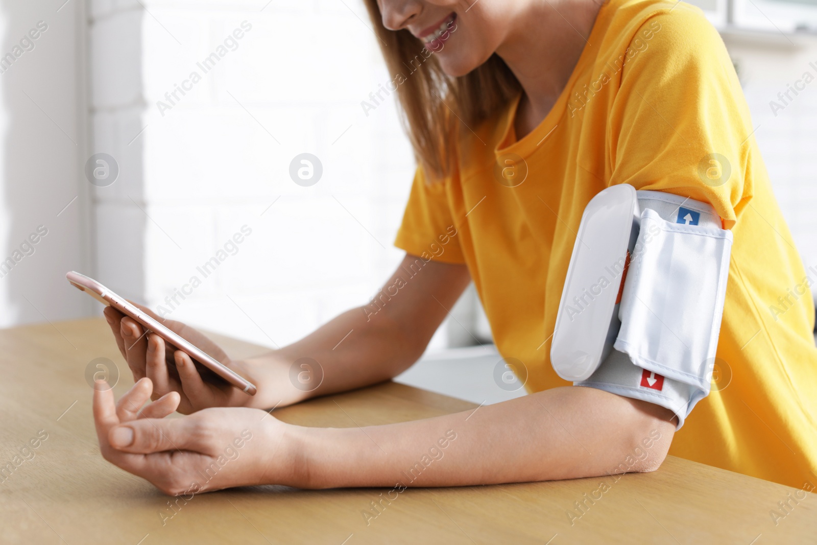 Photo of Woman checking blood pressure with modern monitor and smartphone at table indoors, closeup. Cardiology concept