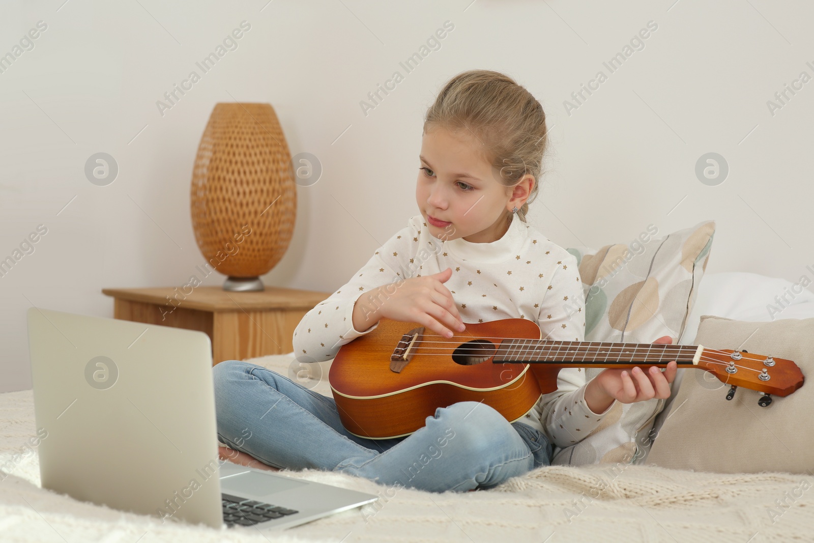 Photo of Little girl learning to play ukulele with online music course at home. Time for hobby