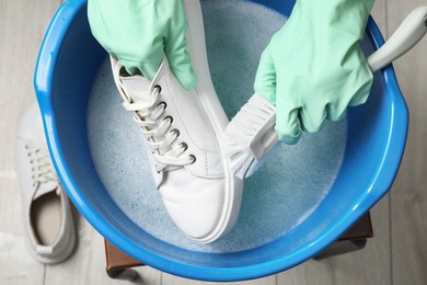 Woman with gloves and brush cleaning stylish sneakers in wash basin, top view