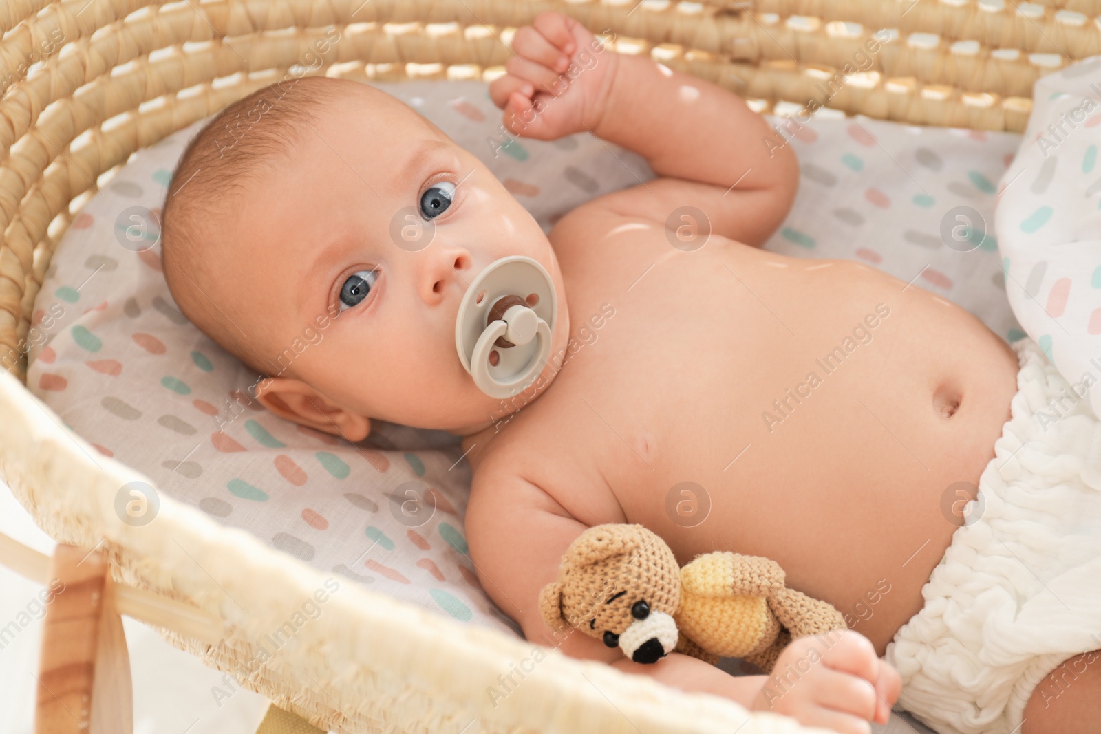 Photo of Cute little baby with pacifier and toy bear lying in cradle
