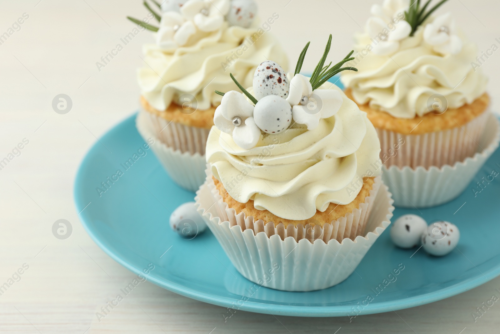 Photo of Tasty Easter cupcakes with vanilla cream on light wooden table, closeup