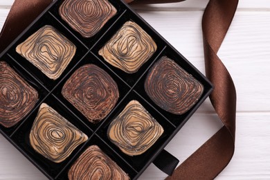 Box of tasty chocolate candies and ribbon on white wooden table, top view