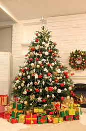 Photo of Decorated Christmas tree with gift boxes and fireplace in room