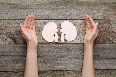 Woman protecting paper cutout of kidneys at wooden table, top view