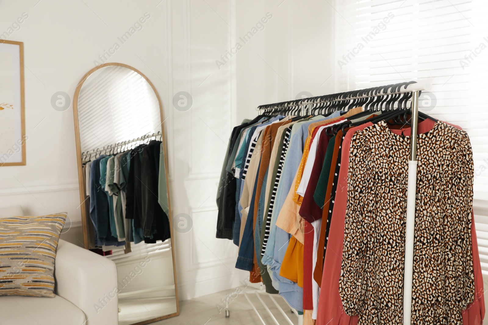 Photo of Rack with stylish clothes near sofa and mirror indoors. Fast fashion