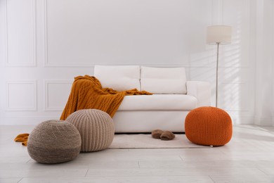Stylish living room interior with white sofa and knitted poufs
