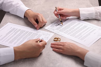 Photo of Man and woman signing marriage contract at light grey table, closeup