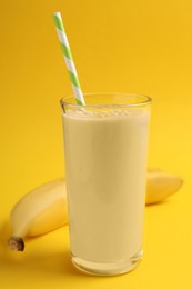 Glass of tasty banana smoothie with straw and fresh fruit on yellow background