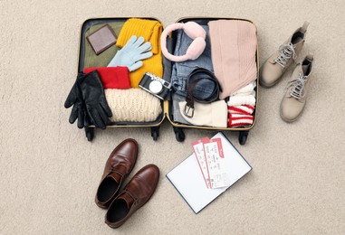 Open suitcase with warm clothes, accessories and shoes on floor, flat lay