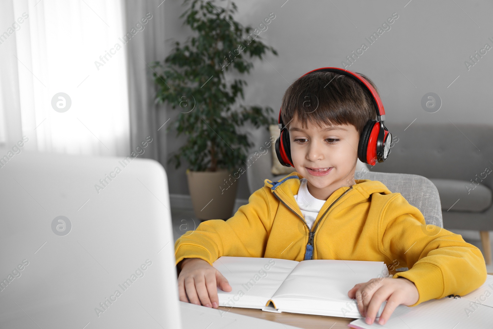 Photo of Cute little boy with modern laptop studying online at home. E-learning