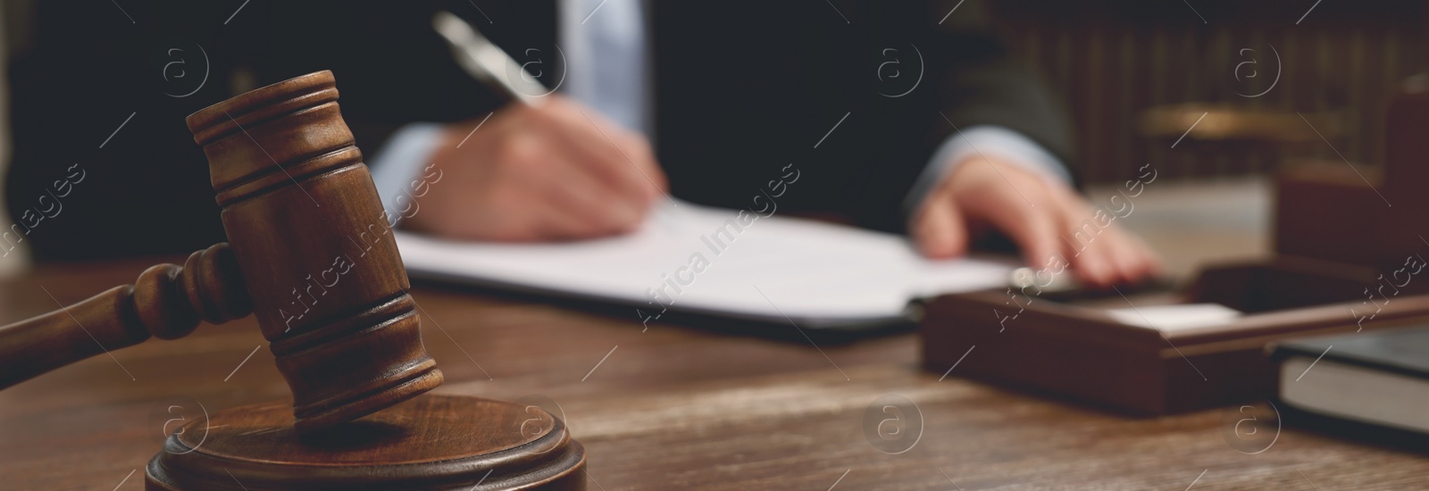 Image of Lawyer working with document at wooden table in office, focus on gavel. Banner design