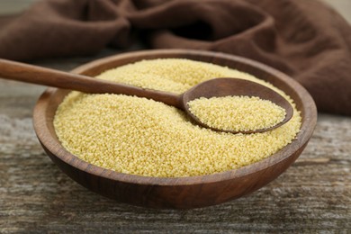 Photo of Bowl and spoon with raw couscous on wooden table, closeup