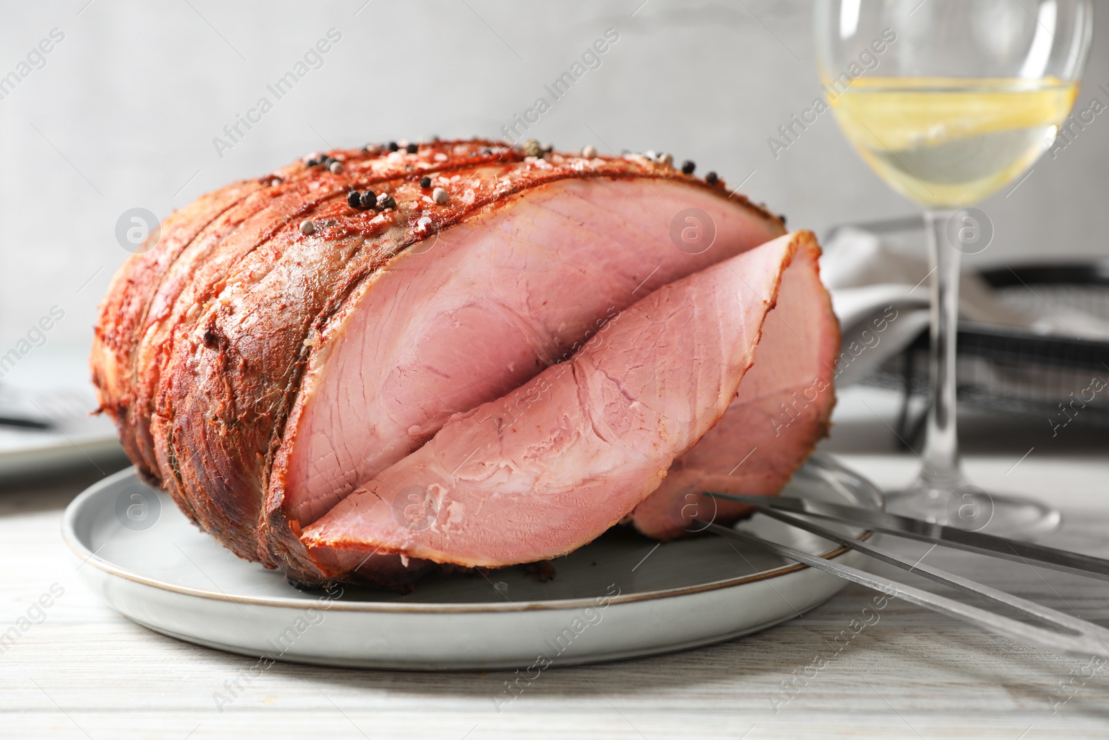 Photo of Delicious baked ham, carving fork, knife and glass of drink on white wooden table, closeup