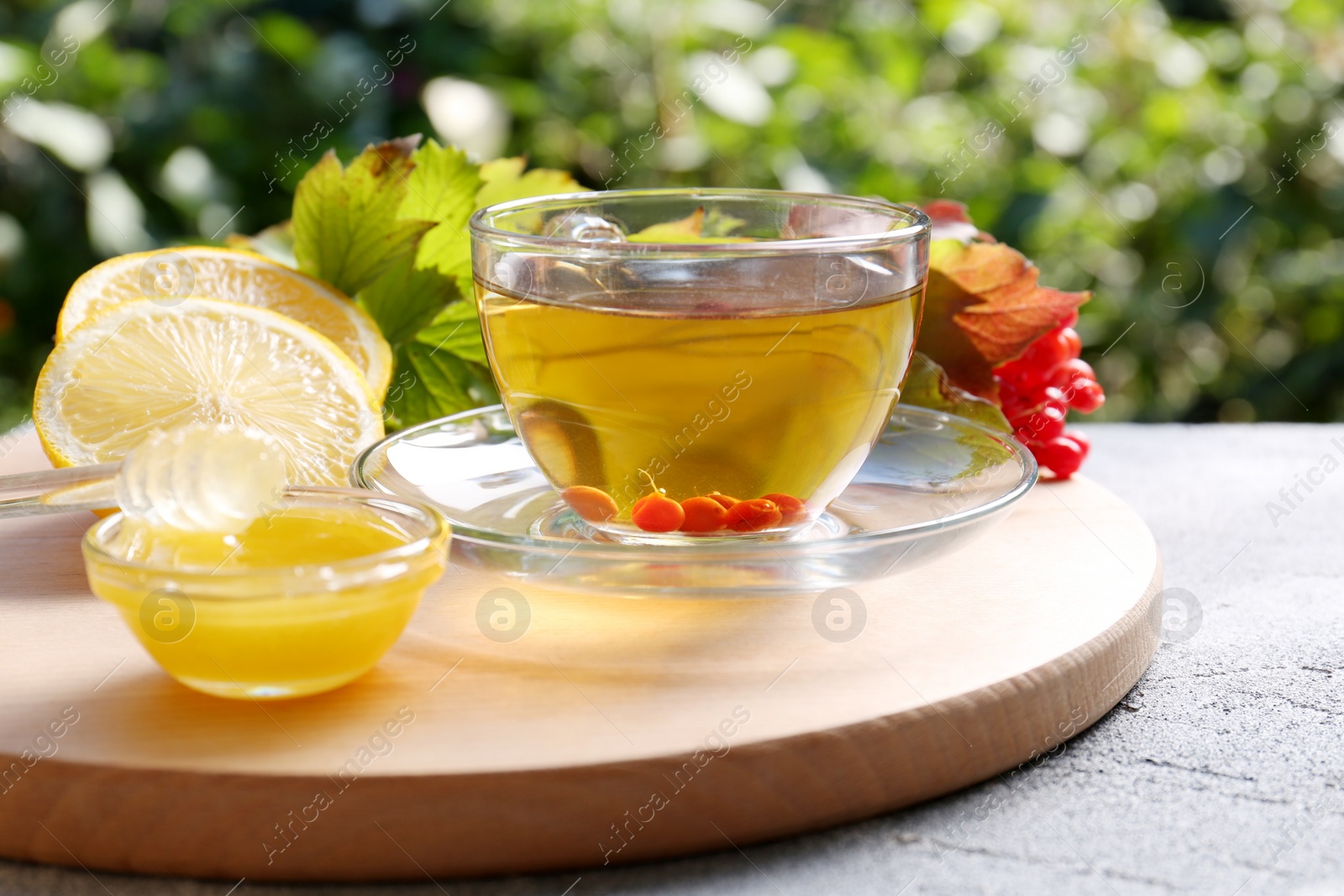 Photo of Cup of delicious tea with lemon, honey and viburnum on light grey table outdoors