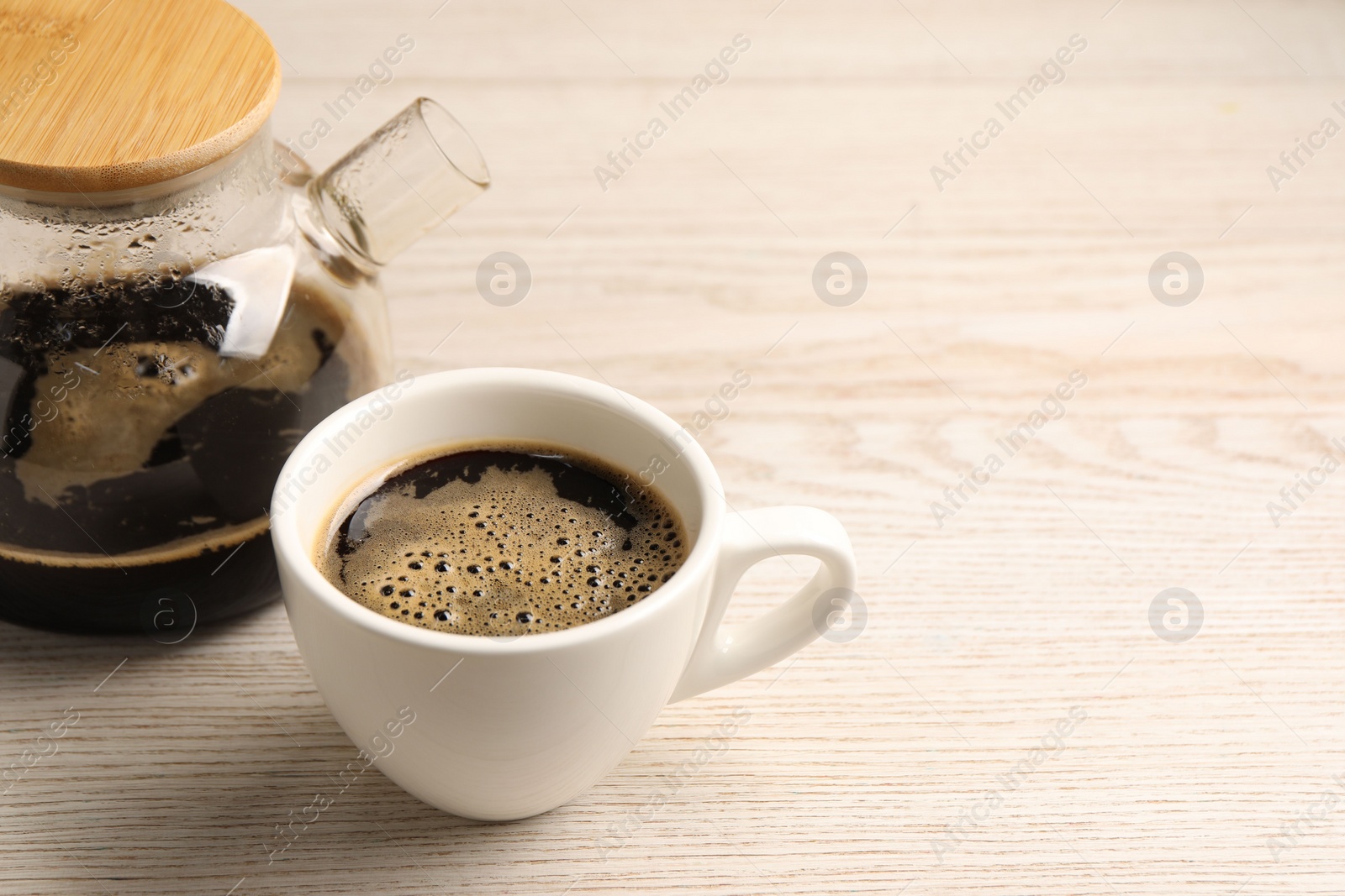 Photo of Aromatic coffee in cup and teapot on light wooden table, closeup. Space for text