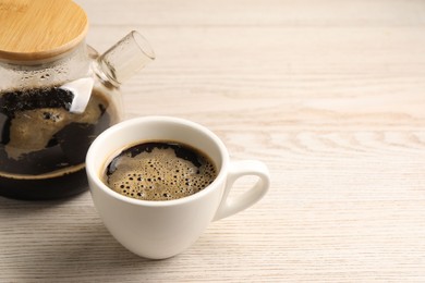 Photo of Aromatic coffee in cup and teapot on light wooden table, closeup. Space for text