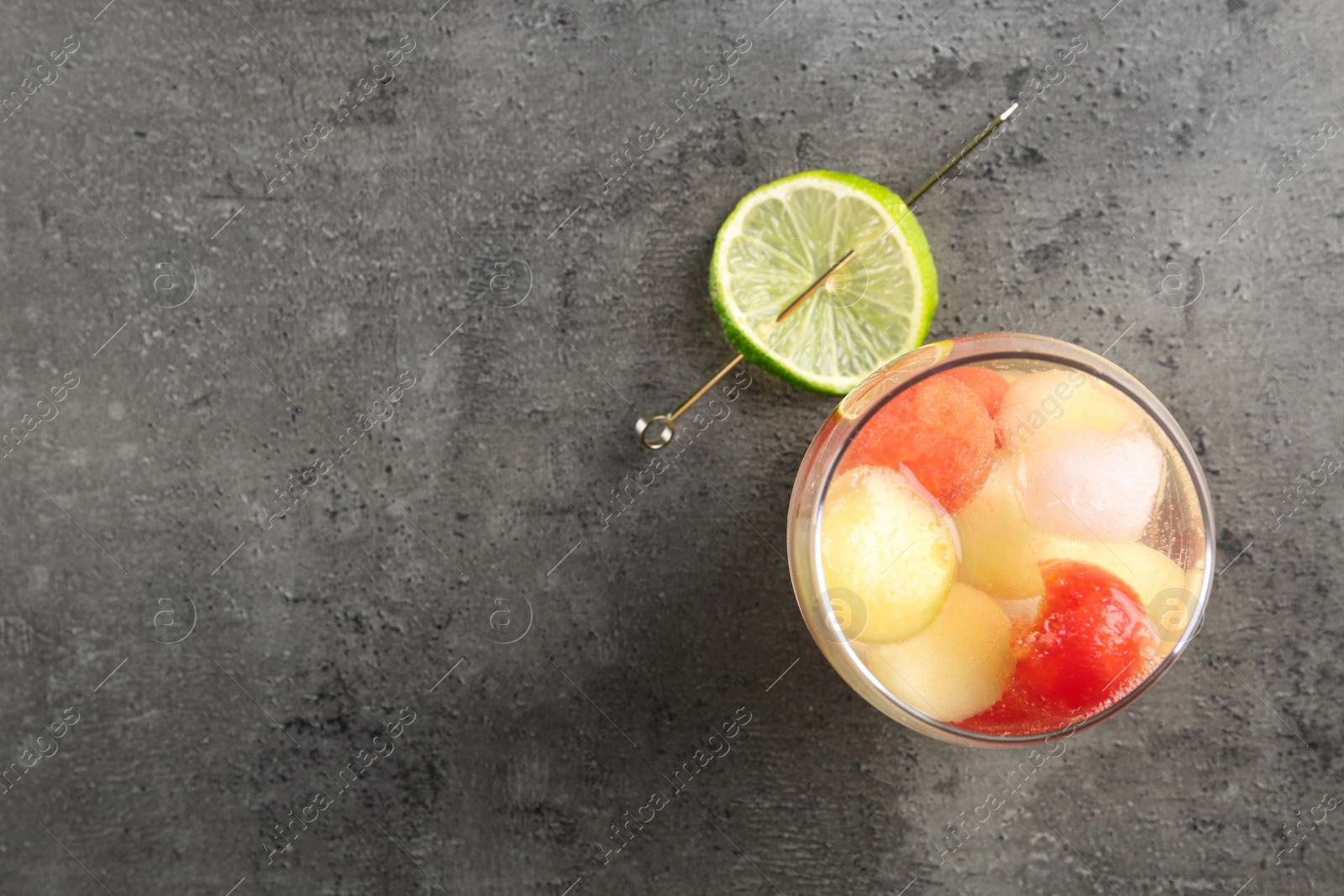 Photo of Glass of melon and watermelon ball cocktail with lime on grey table, flat lay. Space for text