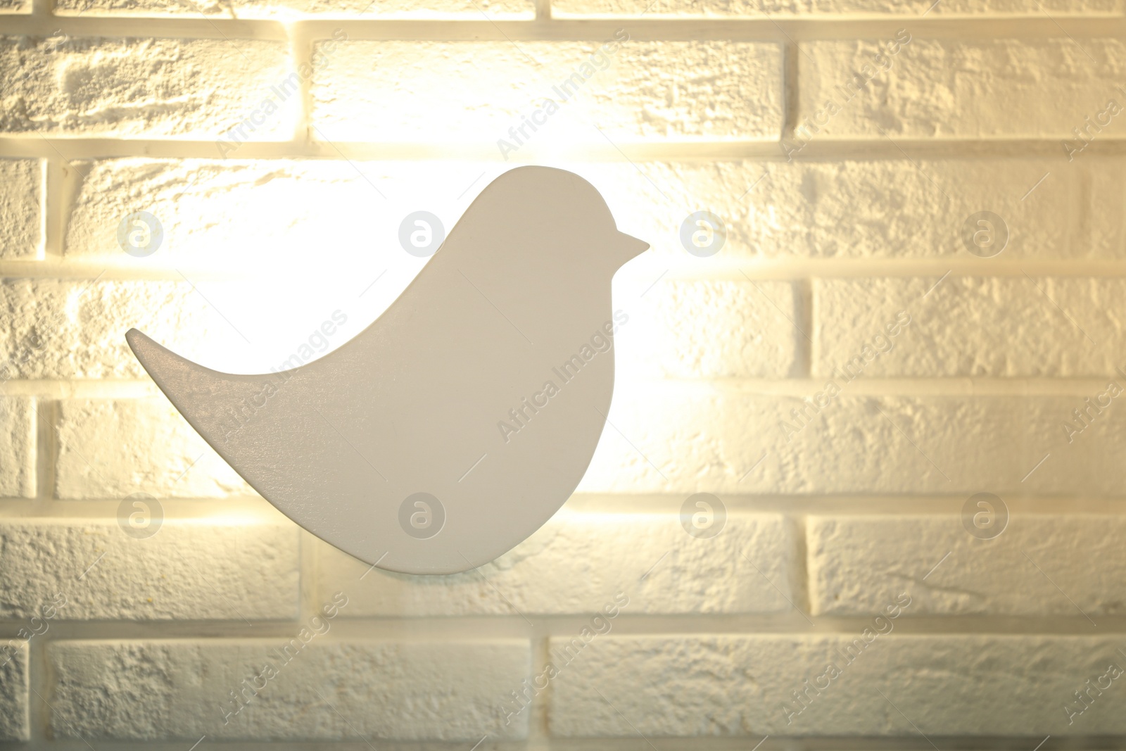 Photo of Bird shaped night lamp on white brick wall. Space for text