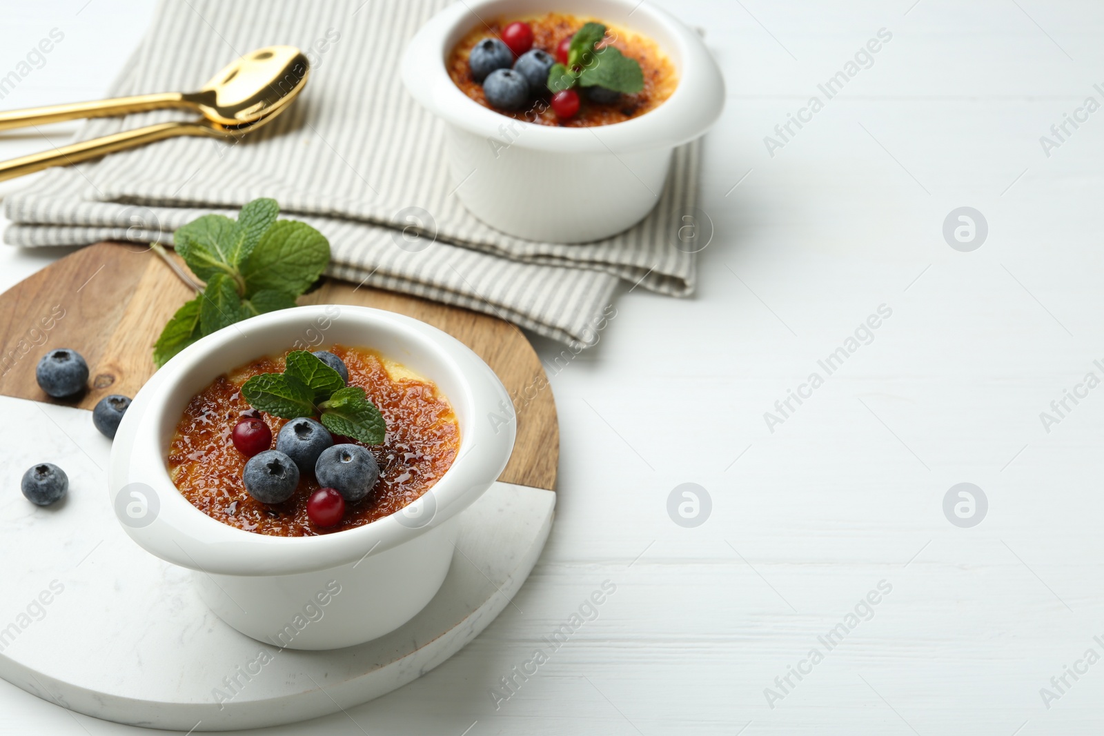 Photo of Delicious creme brulee with berries and mint in bowls on white wooden table, closeup. Space for text