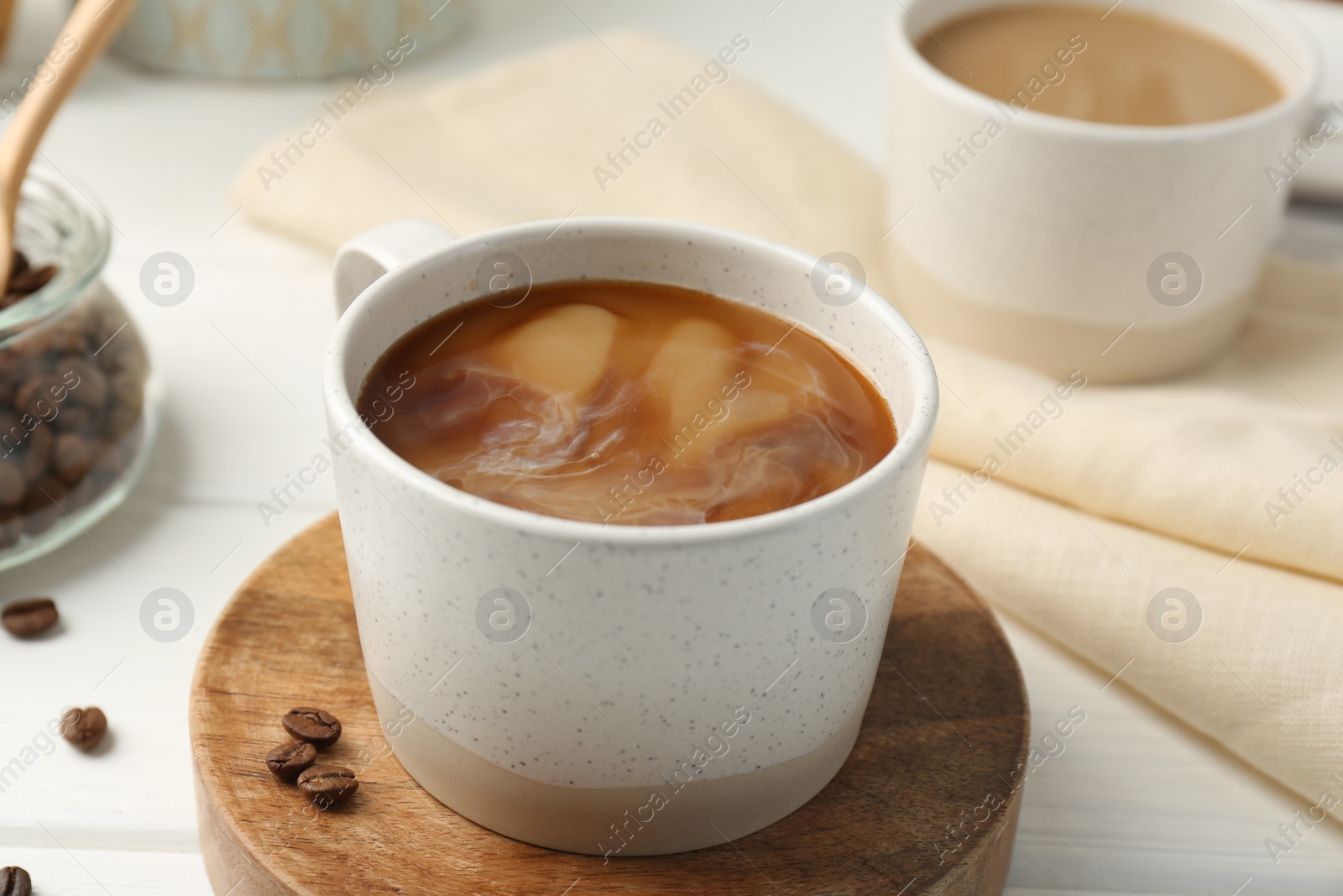 Photo of Aromatic coffee with milk in cup and beans on white wooden table, closeup