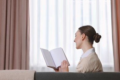 Photo of Woman reading book on sofa near window with stylish curtains at home. Space for text
