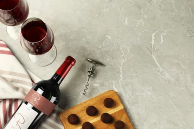 Glasses and bottle of red wine with chocolate on light marble table, flat lay. Space for text