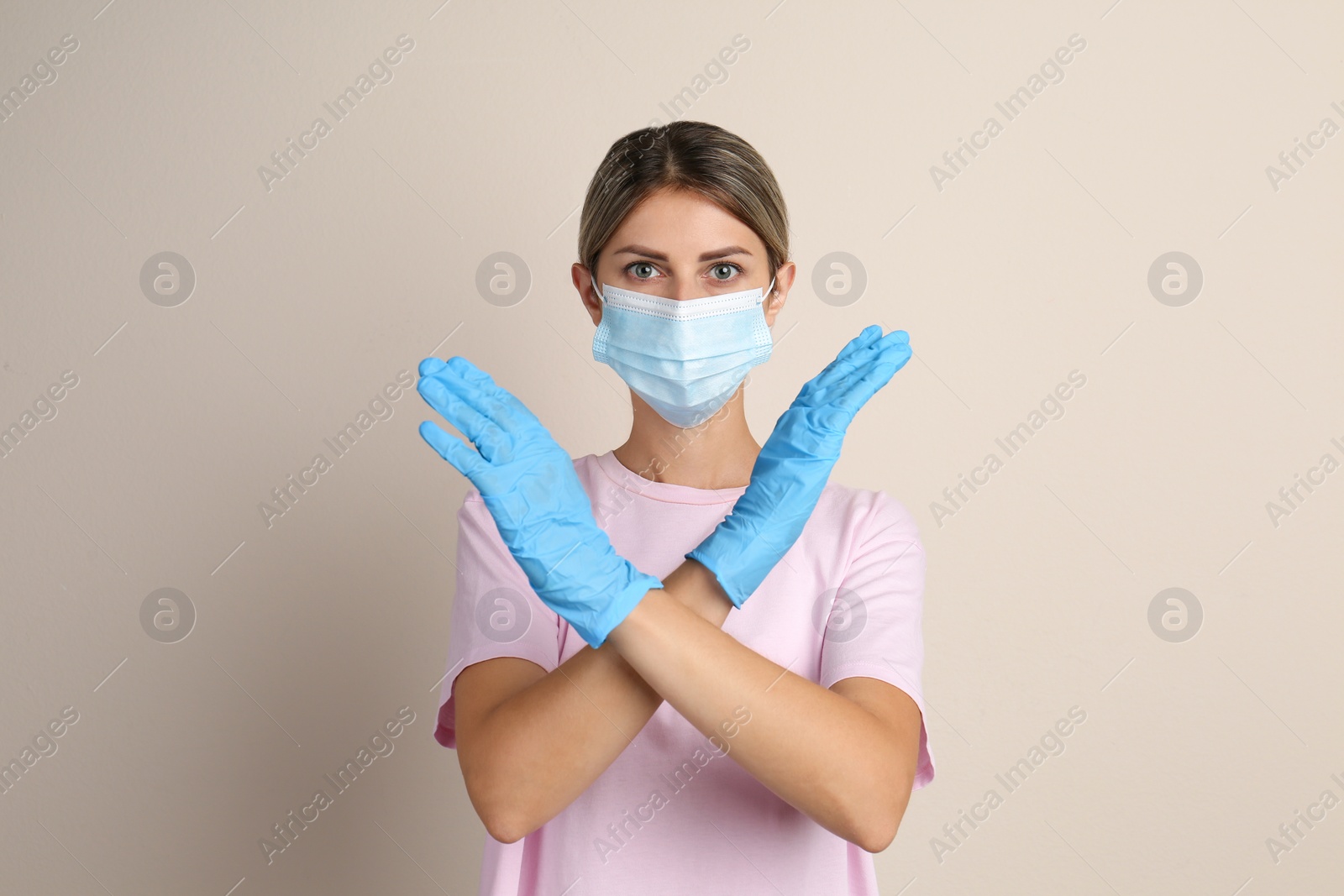 Photo of Woman in protective mask showing stop gesture on beige background. Prevent spreading of COVID‑19