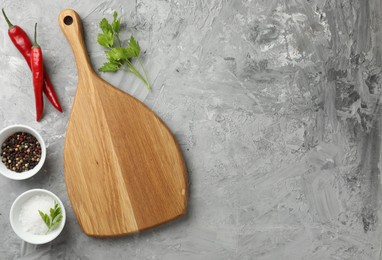 Photo of Cutting board, salt, spices, chili peppers and parsley on grey textured table, flat lay. Space for text