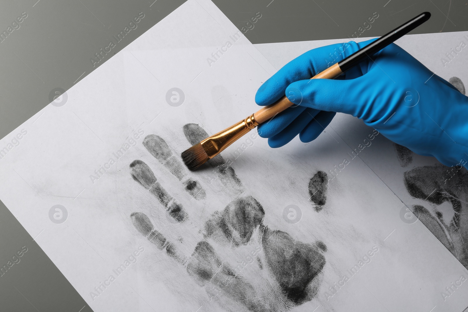 Photo of Detective taking fingerprints with brush from paper on grey background, top view.  Criminal investigation