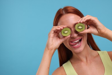 Funny woman covering eyes with halves of fresh kiwi and showing tongue on light blue background, space for text