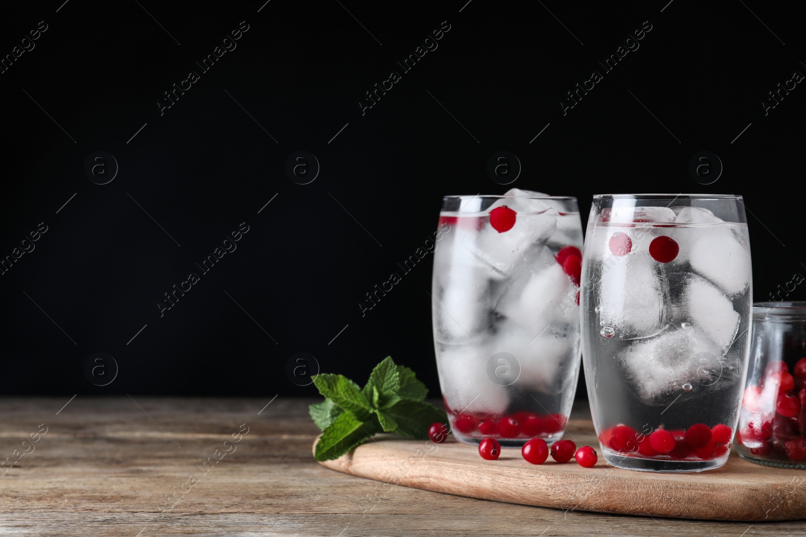 Photo of Glasses of cocktail with vodka, ice and cranberry on wooden table against black background. Space for text