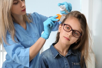 Photo of Doctor using nit comb and spray on girl's hair indoors. Anti lice treatment