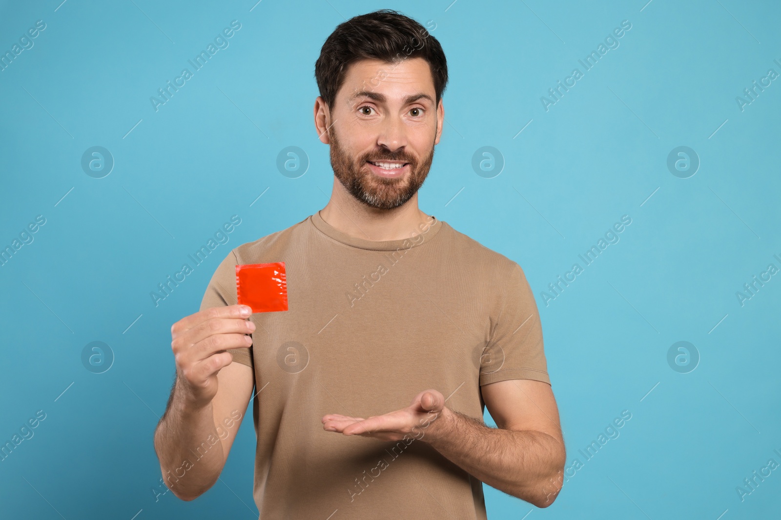 Photo of Happy man holding condom on light blue background. Safe sex