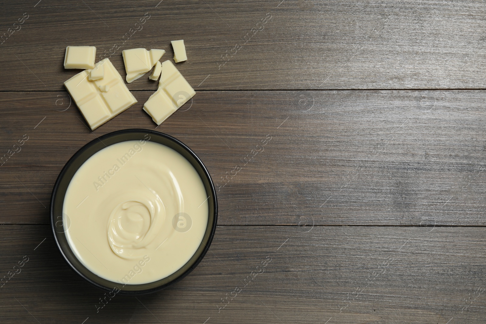 Photo of Tasty white chocolate paste in bowl and pieces on wooden table, top view. Space for text