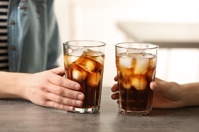 Women holding glasses of cola with ice at table, closeup