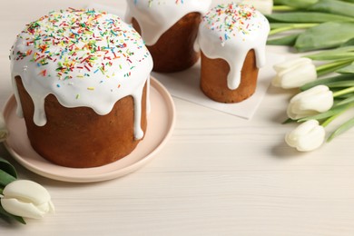 Photo of Delicious Easter cakes with sprinkles and beautiful tulips on white wooden table. Space for text