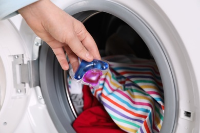 Photo of Woman putting laundry detergent capsule into washing machine, closeup