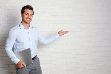 Photo of Young male teacher with laptop near brick wall. Space for text