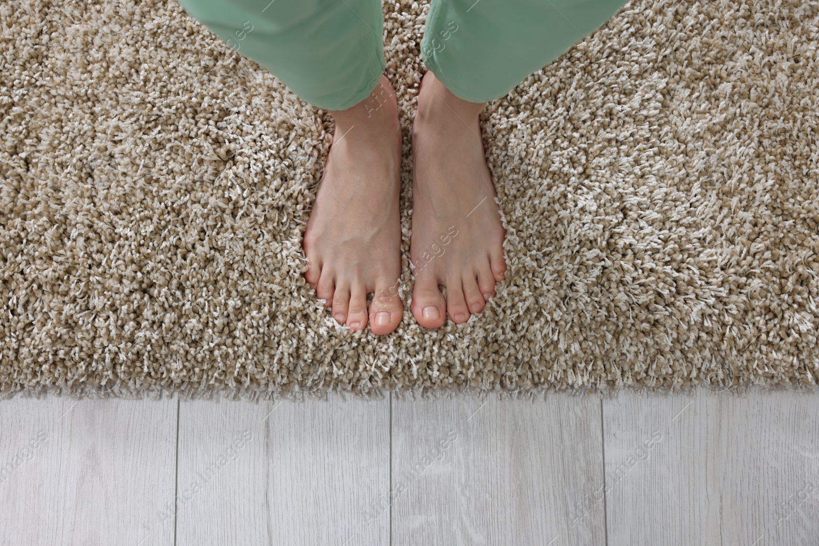 Photo of Woman standing on soft light brown carpet at home, top view