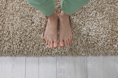 Photo of Woman standing on soft light brown carpet at home, top view