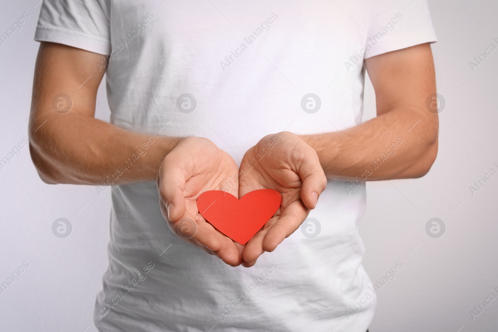 Photo of Young man holding small red heart in hands, closeup