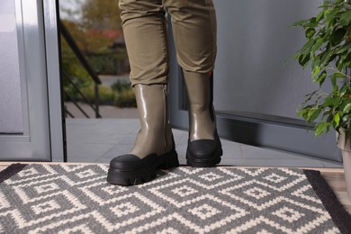 Photo of Woman in stylish boots entering hall with clean door mat on floor, closeup