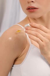 Photo of Woman applying essential oil onto shoulder on blurred background, closeup