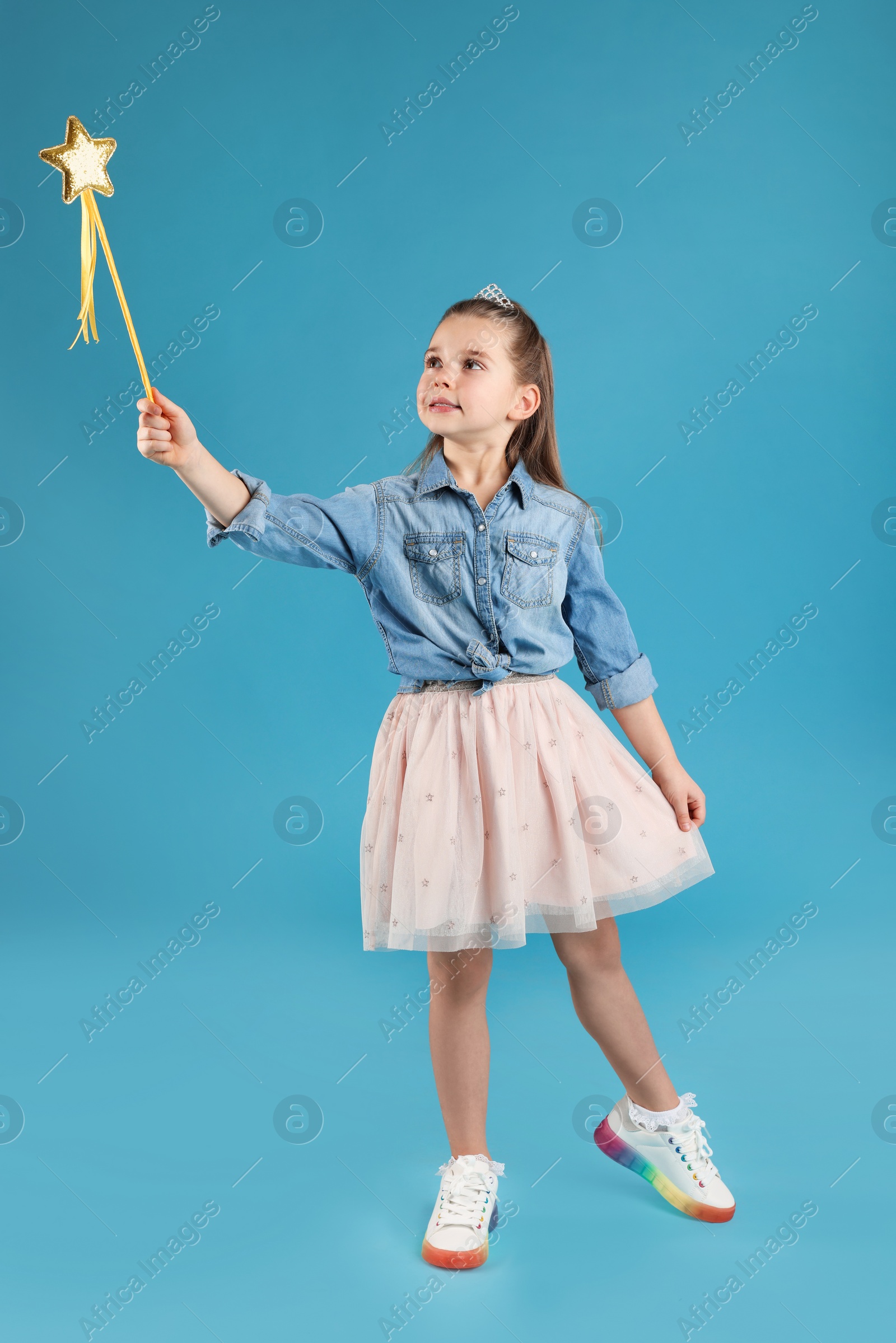 Photo of Cute girl in diadem with magic wand on light blue background. Little princess