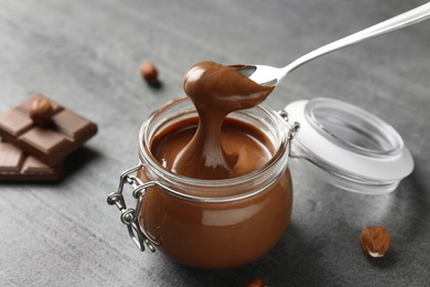 Photo of Spoon with tasty chocolate cream over full jar on table