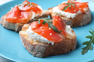 Photo of Delicious sandwiches with cream cheese, salmon and arugula on light blue plate, closeup