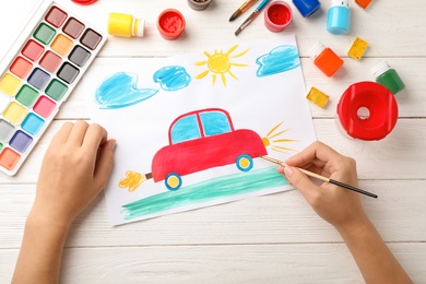 Photo of Girl painting picture of car on table, top view