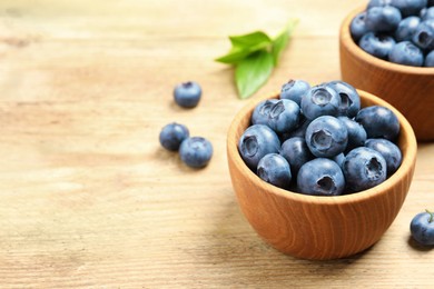 Photo of Bowls of fresh tasty blueberries on wooden table, closeup. Space for text
